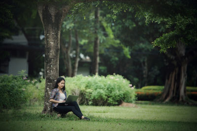 Young woman sitting on bench by tree