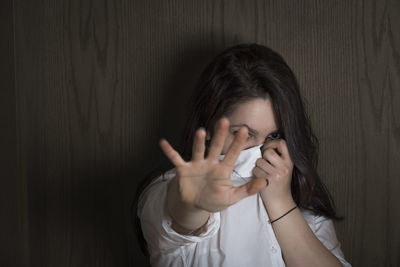 Portrait of woman showing stop gesture against wall