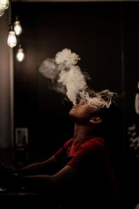 Young man smoking cigarette in dark