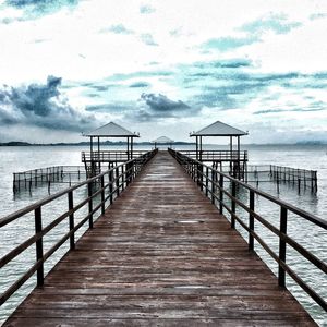 Wooden pier on sea against cloudy sky