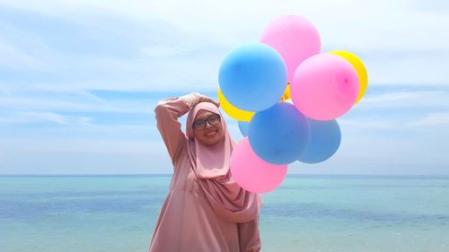 Rear view of young woman with balloons in sea against sky