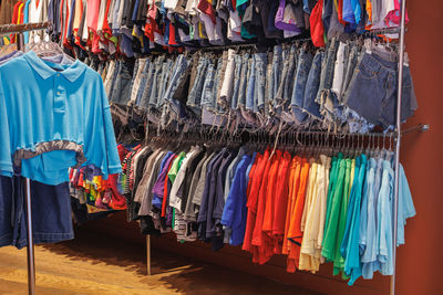 Colorful polo, t-shirts and summer jeans shorts hanging in a coat rack inside a store.