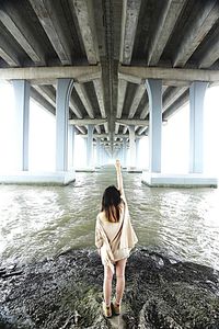 Woman standing on rock in front of river below bridge