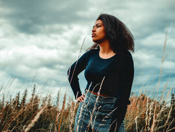 Young woman looking away on field against sky
