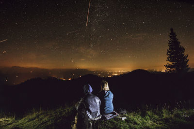 Rear view of couple sitting on mountain against star field at night