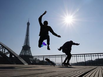 Low angle view of silhouette people skateboarding against eiffel tower on sunny day