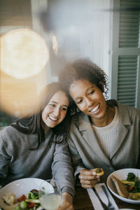 Smiling young female friends sitting at dining table in patio for dinner party