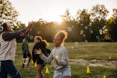 Girl playing amidst bubbles with friends in playground at summer camp