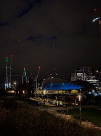 Illuminated train by buildings against sky at night