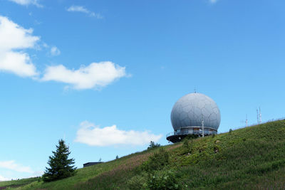 Low angle view of radar tower and grassy hill against blue sky