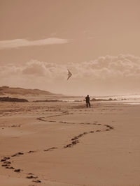 Silhouette person flying over beach against sky