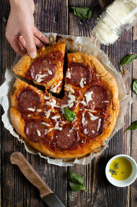 High angle view of hand holding pizza on table