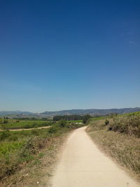 Road passing through field against cloudy sky