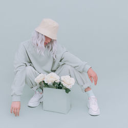 Full length of woman crouching by flowers in box over gray background