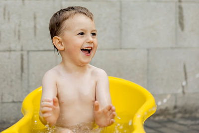 Cute little boy bathing in yellow tub outdoors. happy child is splashing, playing with water 