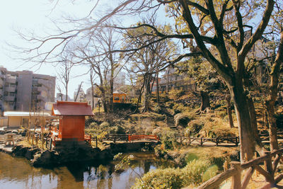 Trees and houses by lake against sky in city