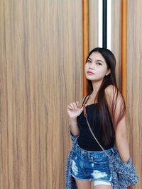 Beautiful young woman standing against wooden wall