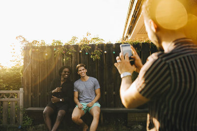 Man photographing friends on smart phone at yard during summer