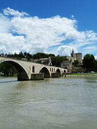 Arch bridge over river by buildings against sky