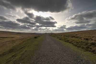 Road passing through landscape against cloudy sky