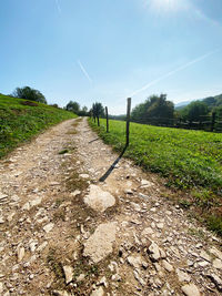 Dirt road amidst field against sky
