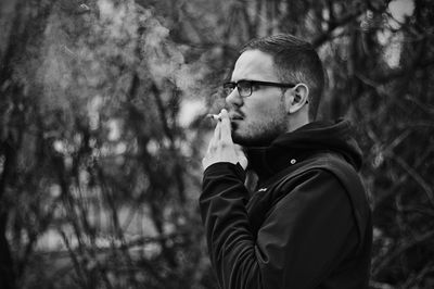 Young man smoking while standing against trees