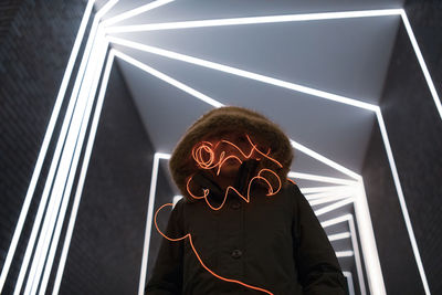 Woman in hooded clothing with light painting standing against illuminated lights