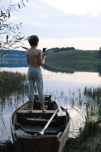 Rear view of boy standing on boat against sky with flying bird