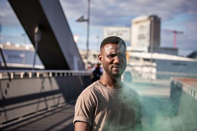 Portrait of young man with smoke standing on bridge