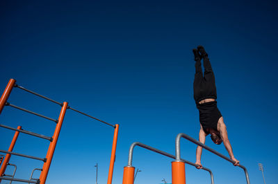 Low angle view of man climbing on railing against clear sky