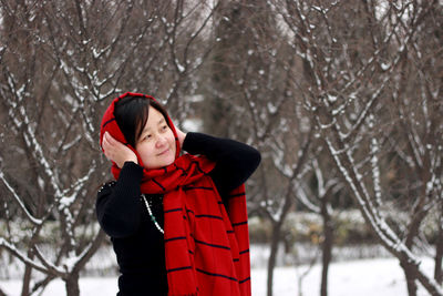 Young woman in warm clothing standing against bare trees