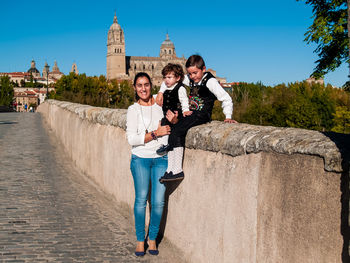 Portrait of smiling woman standing children sitting on wall 