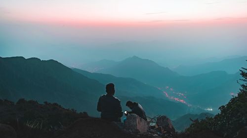 People sitting on mountain against sky during sunset