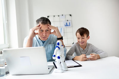 Father and son with toy and laptop on table at home