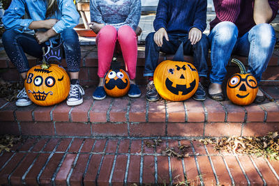 Low section of family sitting with decorated pumpkins on steps during halloween