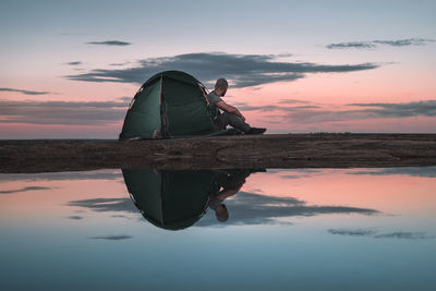 Reflection of man on boat against sky during sunset