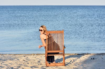 Rear view of woman sitting on chair at beach