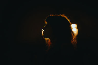 Side view of silhouette woman against illuminated light