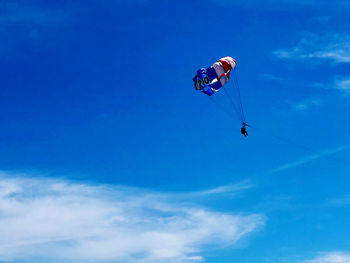 Low angle view of person paragliding against blue sky