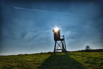 Back lit lookout tower on field against cloudy sky