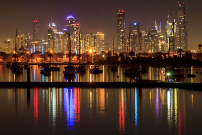 Illuminated buildings reflecting on river against sky at night