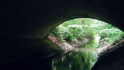 Arch bridge over river seen through tunnel