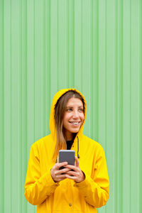 Smiling woman using phone while looking away against green wall