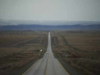 Empty road amidst field against sky