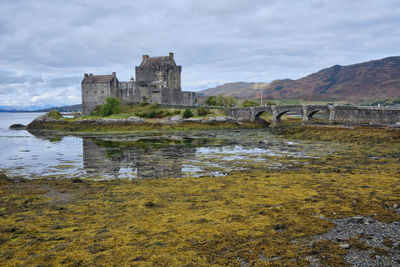 Castle by sea against cloudy sky