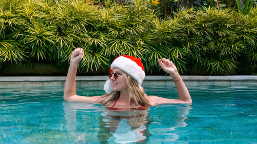 Portrait of woman in christmas mood wearing santa hat and sunglasses in pool. young funny blonde 
