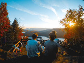 Rear view of people sitting on mountain against sky