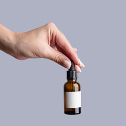 Cropped hand holding bottle against white background