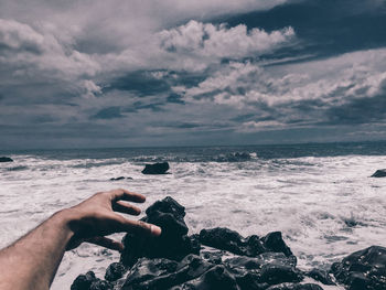Optical illusion of cropped hand reaching for rock against sea