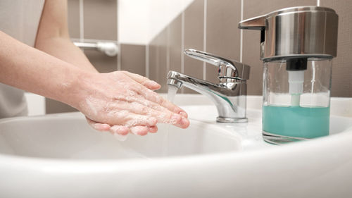Midsection of woman with faucet in kitchen
